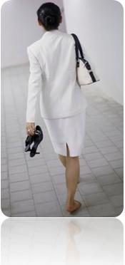 mulher usa vestido tailler anda descalça segura sapatos apertados num corredor de prédio